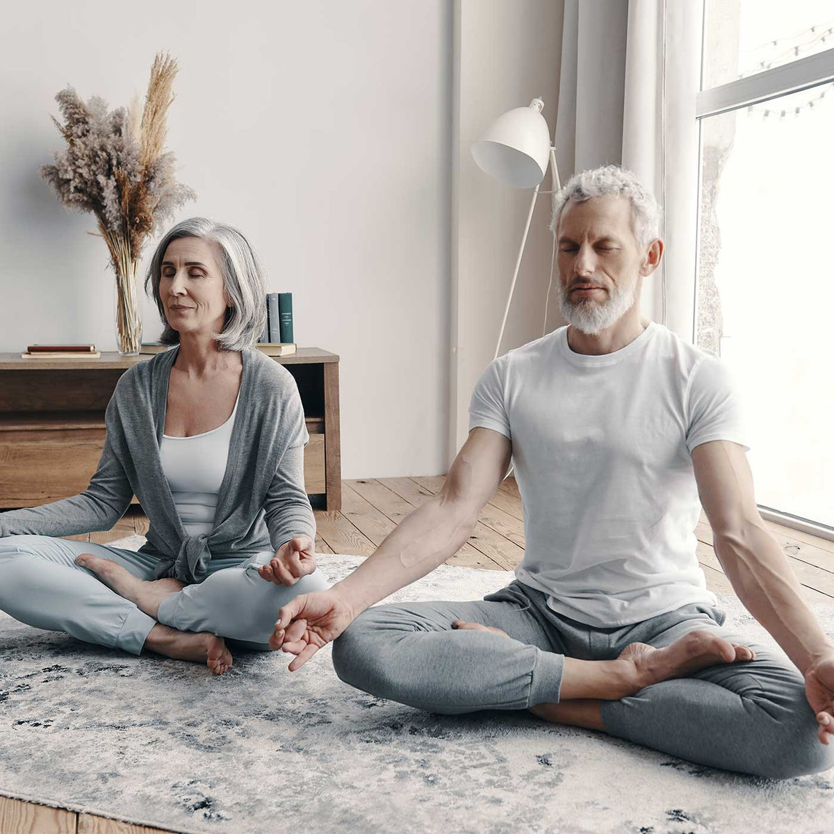 Bone and Joint Health Older man and women sitting side by side cross-legged on a carpet.