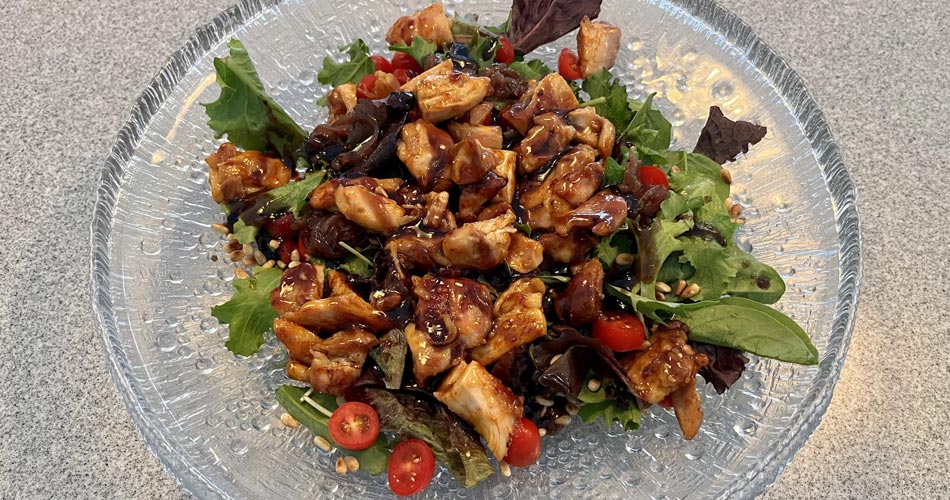 Bowl of salad with romaine, cherry tomatoes, and chicken in brown sauce.
