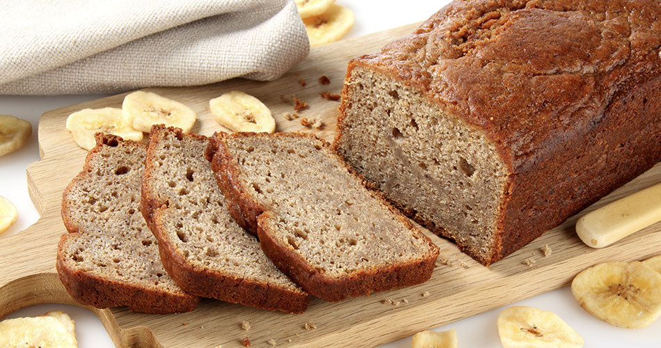 Wooden cutting board with loaf of banana bread and banana slices around it.