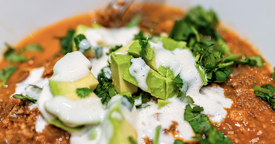 Taco beef soup topped with sour cream, avocado, and greens