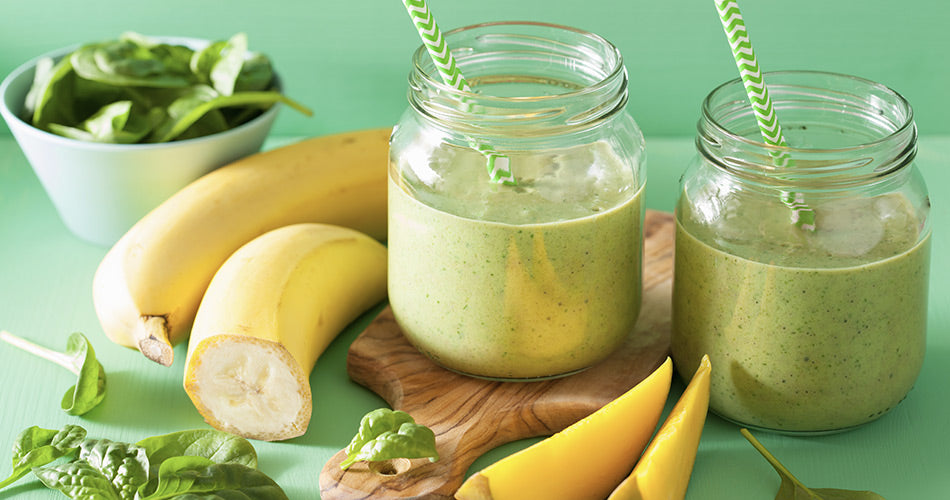 photo showing sliced bananas, mango slices, spinach and the blended shake in two cups with straws