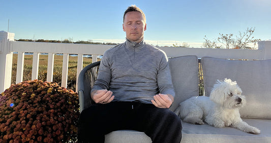 Bjorn Skulason sitting on a couch outside, meditating with a small white dog sitting next to him.