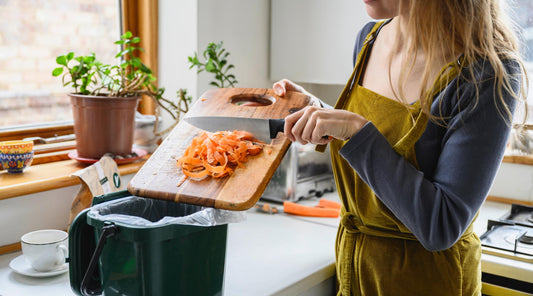 woman putting carrot shavings in compost bin | We can all contribute to a more sustainable world through small, impactful actions—shopping local, reducing food waste, using leftovers, and composting.