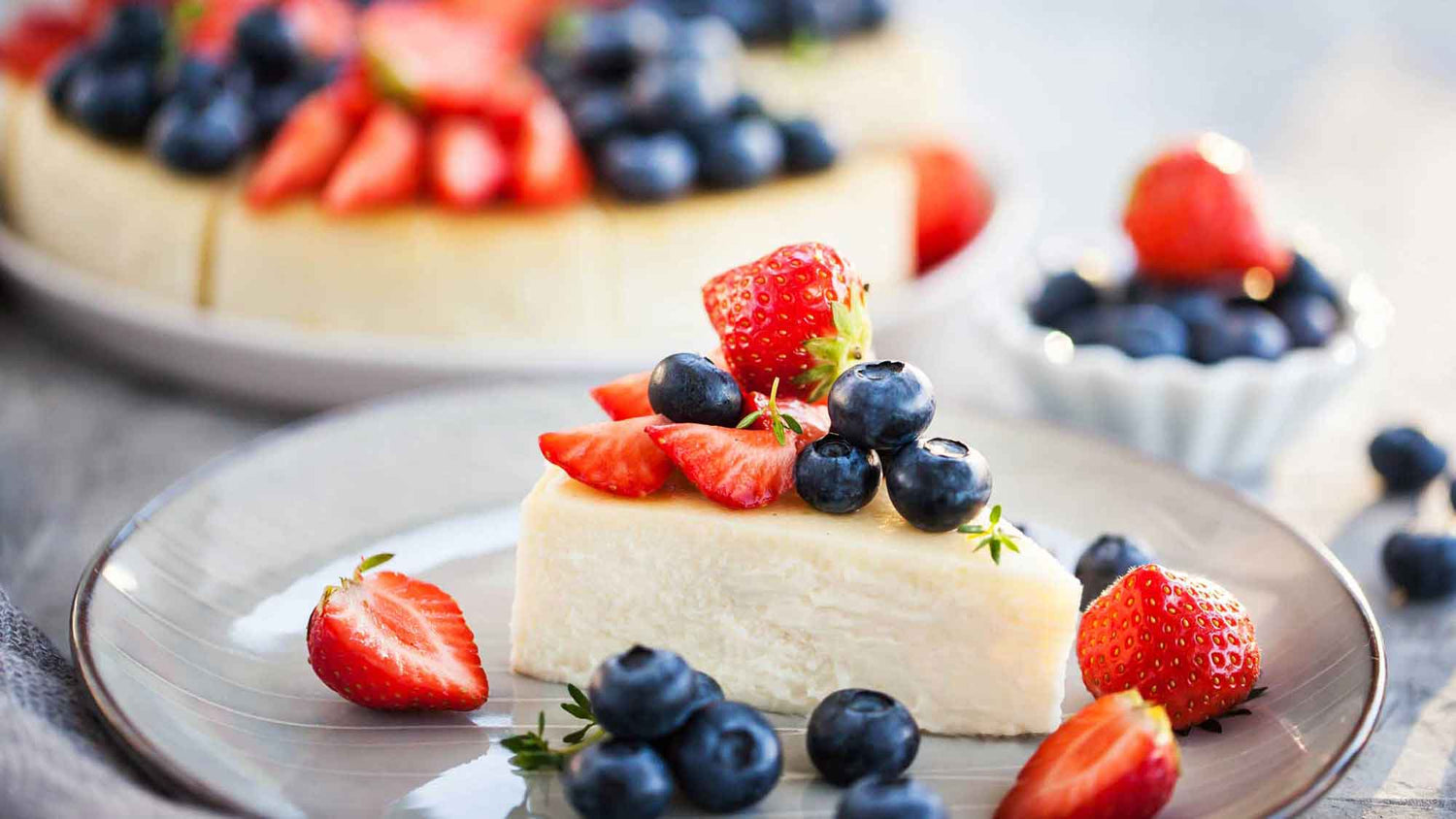Cheesecake on a plate with cut strawberries and blueberries on top.