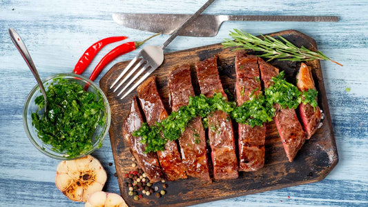 Sliced juicy beef steak with chimichurri sauce and spices on wooden board