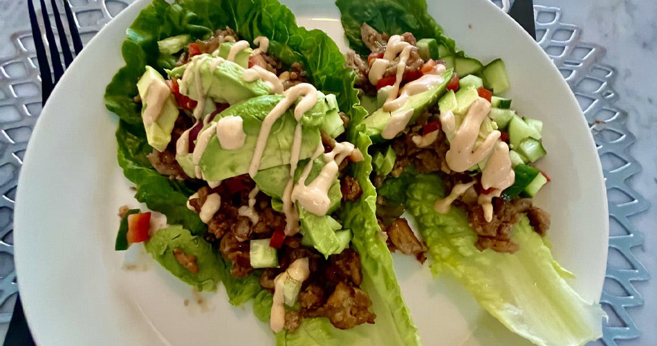 Two lettuce leaves with chicken, avocado, and sauce drizzled on top.