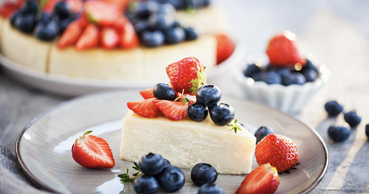 Cheesecake on a plate with cut strawberries and blueberries on top.