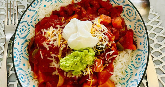Bowl of vegetarian chili topped with dollop of sour cream, guacamole, and shredded cheese.
