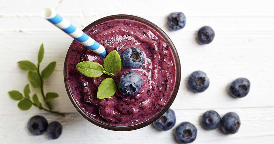 Glass of berry smoothie topped with blueberries and sprig of herbs